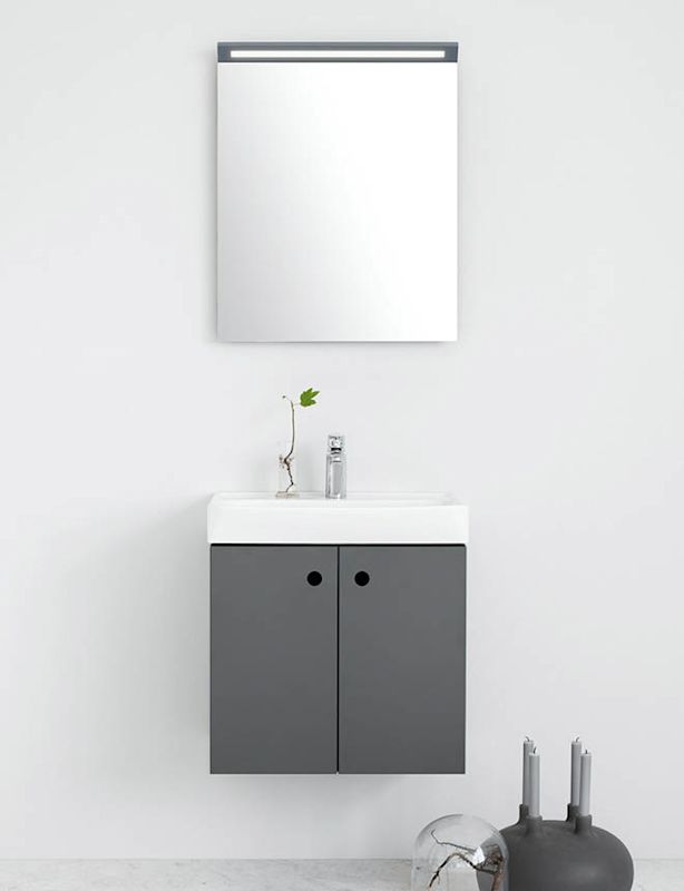 Vit vägg, grå kommod med vitt handfat, fyrkantig spegel, kvist i vas och grå ljusstake.