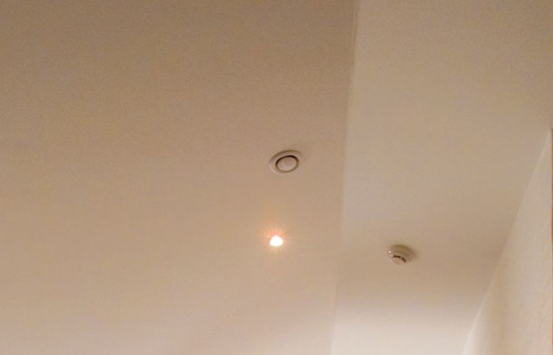 Vitt innertak med varmtonad infälld spot, rund ventil och brandvarnare