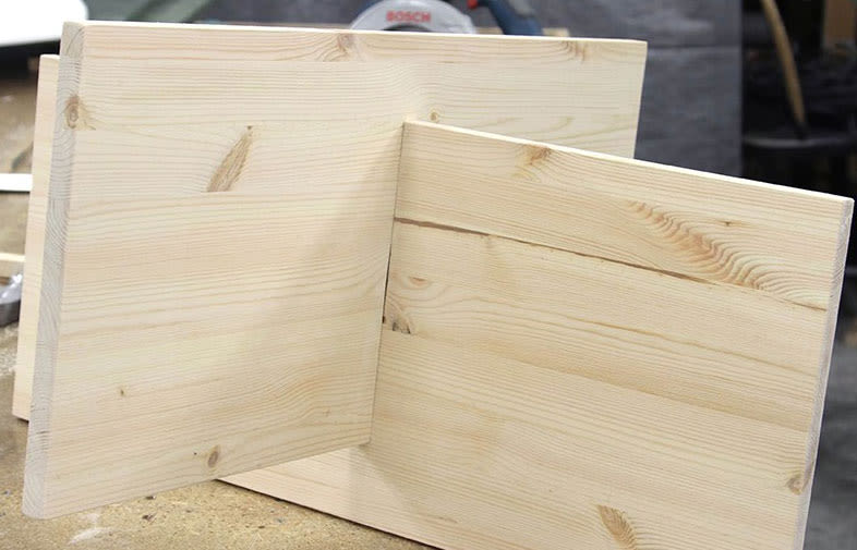 Två ljusa träplankor i L-form på snickarbänk, Bosch-såg i bakgrunden.