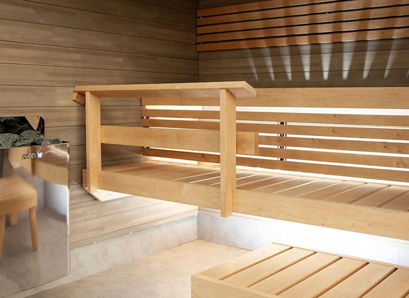 Ljust träinteriör i modern bastu med flera våningsbänkar, dold LED-belysning och rostfri värmekamin