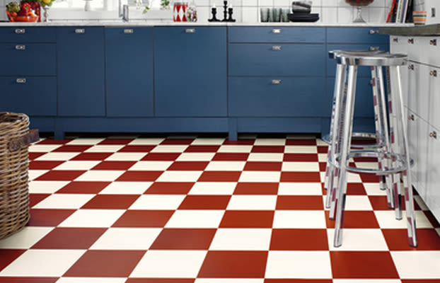 Kök med rödvit schackrutigt golv, blå skåpluckor, kromade barstolar och rottingkorg.