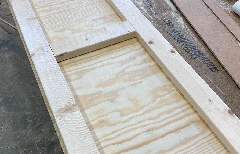 Omonterad ljus plywoodskiva inramad av granregel på verkstadsgolv med sågspån