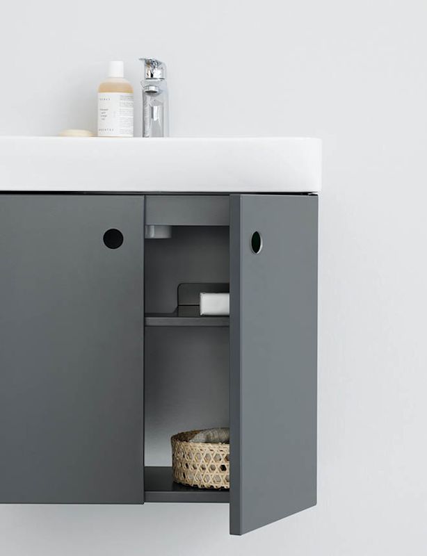 Vit handfat med kromblandare på grått väggskåp med öppna luckor, tvålflaska och rottingkorg.