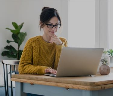 woman in a yellow sweater sitting at a laptop