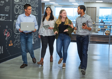 a group of 4 people walking holding mobile devices and chatting