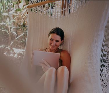woman sitting on a hammock while looking at a tablet