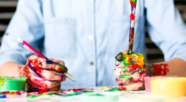 image of person holding paint brushes with paint on hands