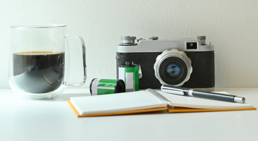 Image of a camera on a desk next to a cup of coffee and a journal