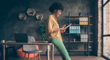 woman looking at a tablet while leaning against a desk