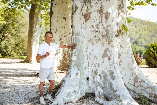 Winemaker Monsieur Xavier Paul stands leaning beside a tree with a glass in hand