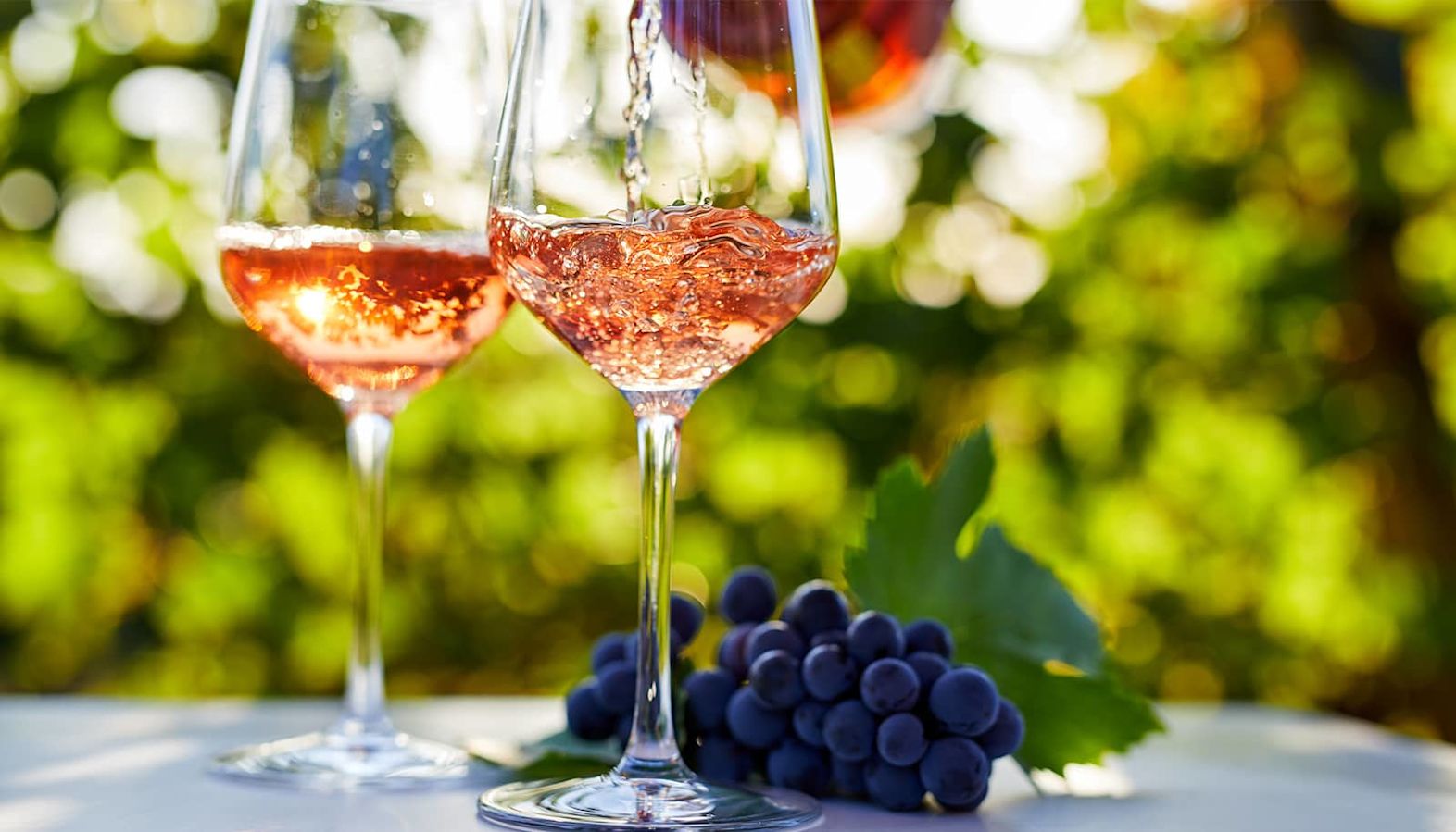 Two glasses of sweet rosé wine with grapes outside on a table in a vineyard - which wines are sweet