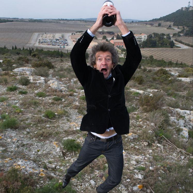 Winemaker Gérard Bertrand leaps into the air holding a bottle of red wine above his head