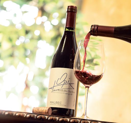 Red wine being poured into glass next to bottle of Opi Malbec