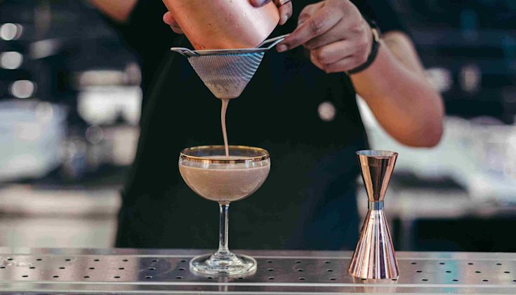 A barman straining a Nutty Irishman cocktail into a glass