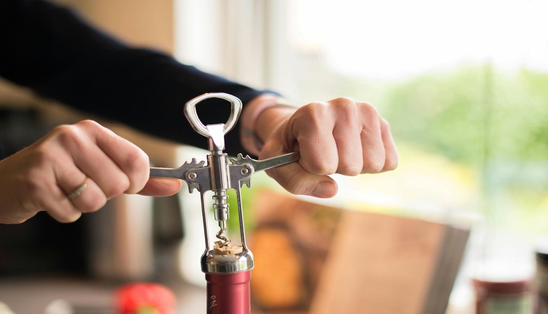 A person using a wine corkscrew to remove a cork from a bottle