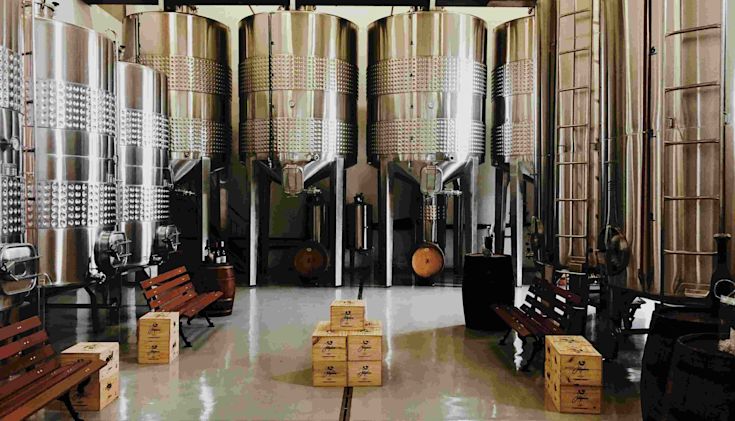 A clean spacious room with wooden crates and stainless steel brewing tanks