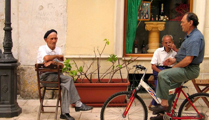 Three men in outside a bar in Puglia – two seated and one on a bycicle