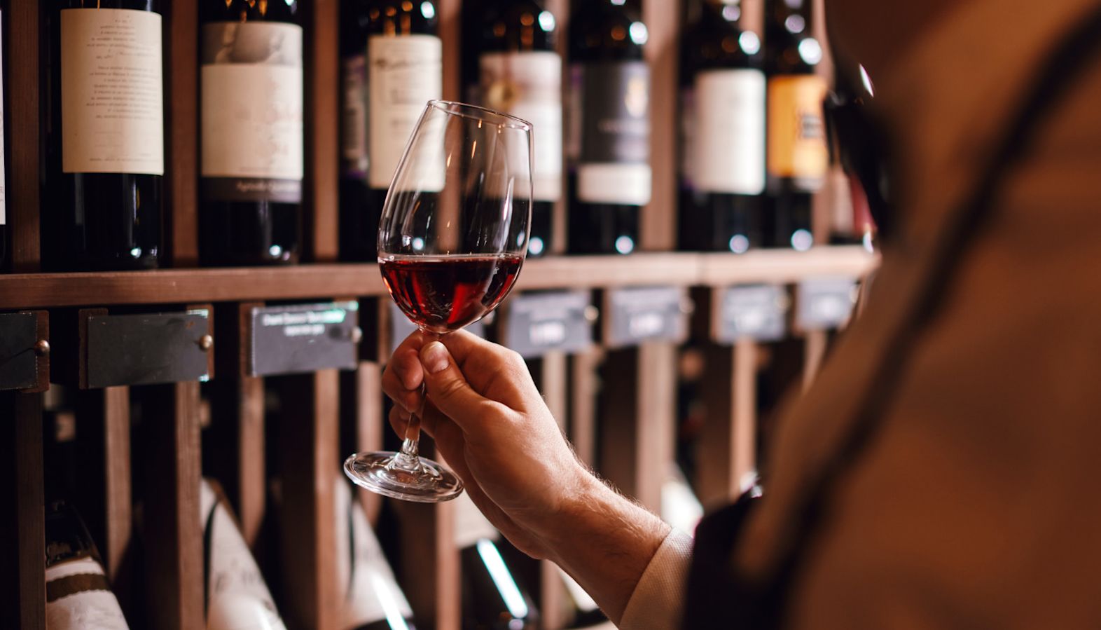 A vintner holding a glass of red wine in a wine cellar - wine ratings