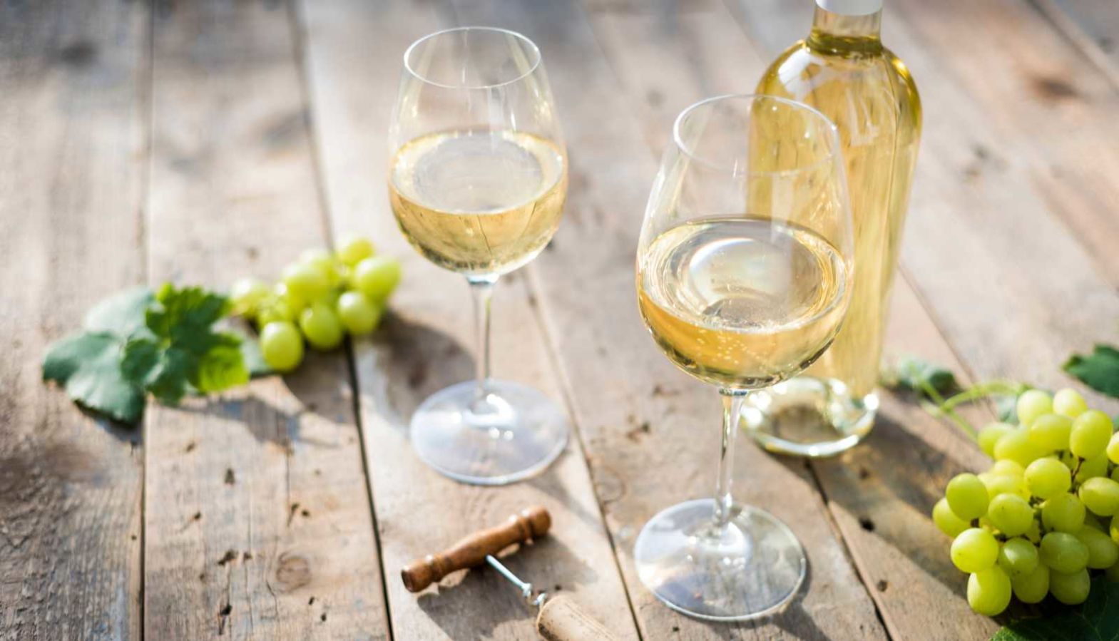A bottle of white wine and two glasses on a wooden table - types of white wine