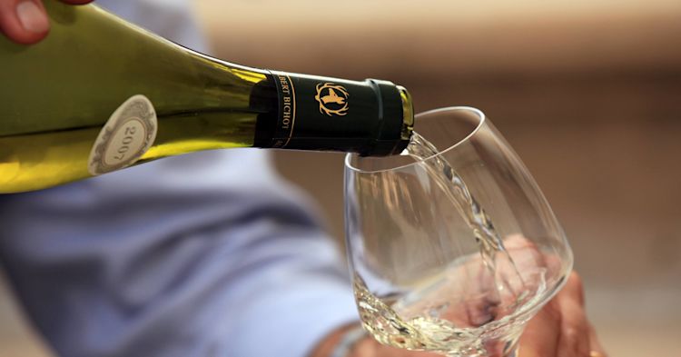 Close up of a white wine in a Burgundy style bottle being poured into a glass.