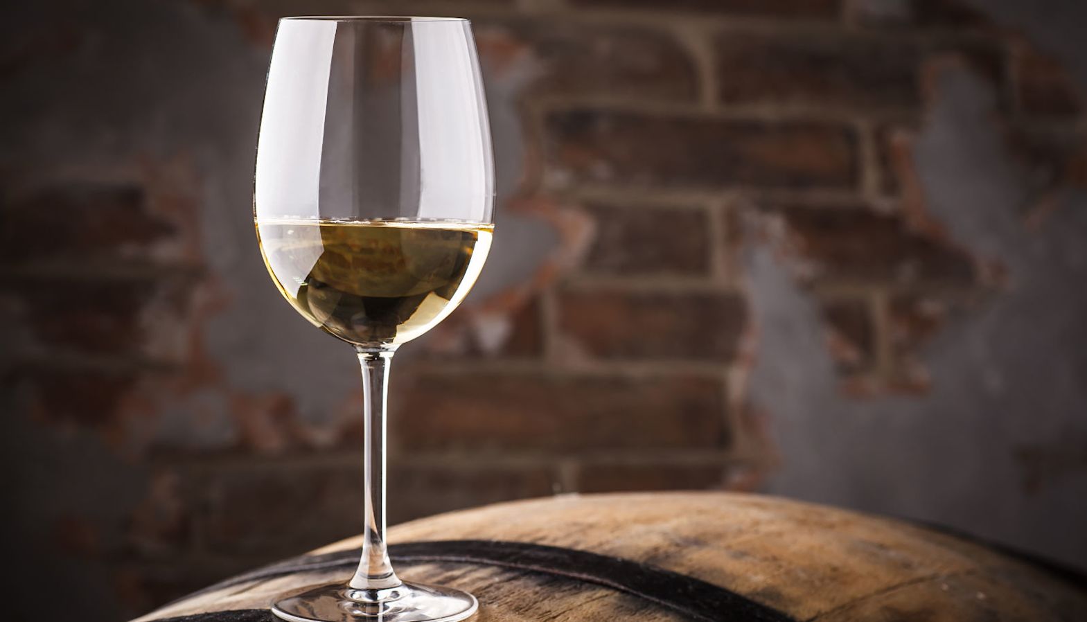 A glass of Chardonnay sitting on top of a barrel in a wine cellar - oaked Chardonnay