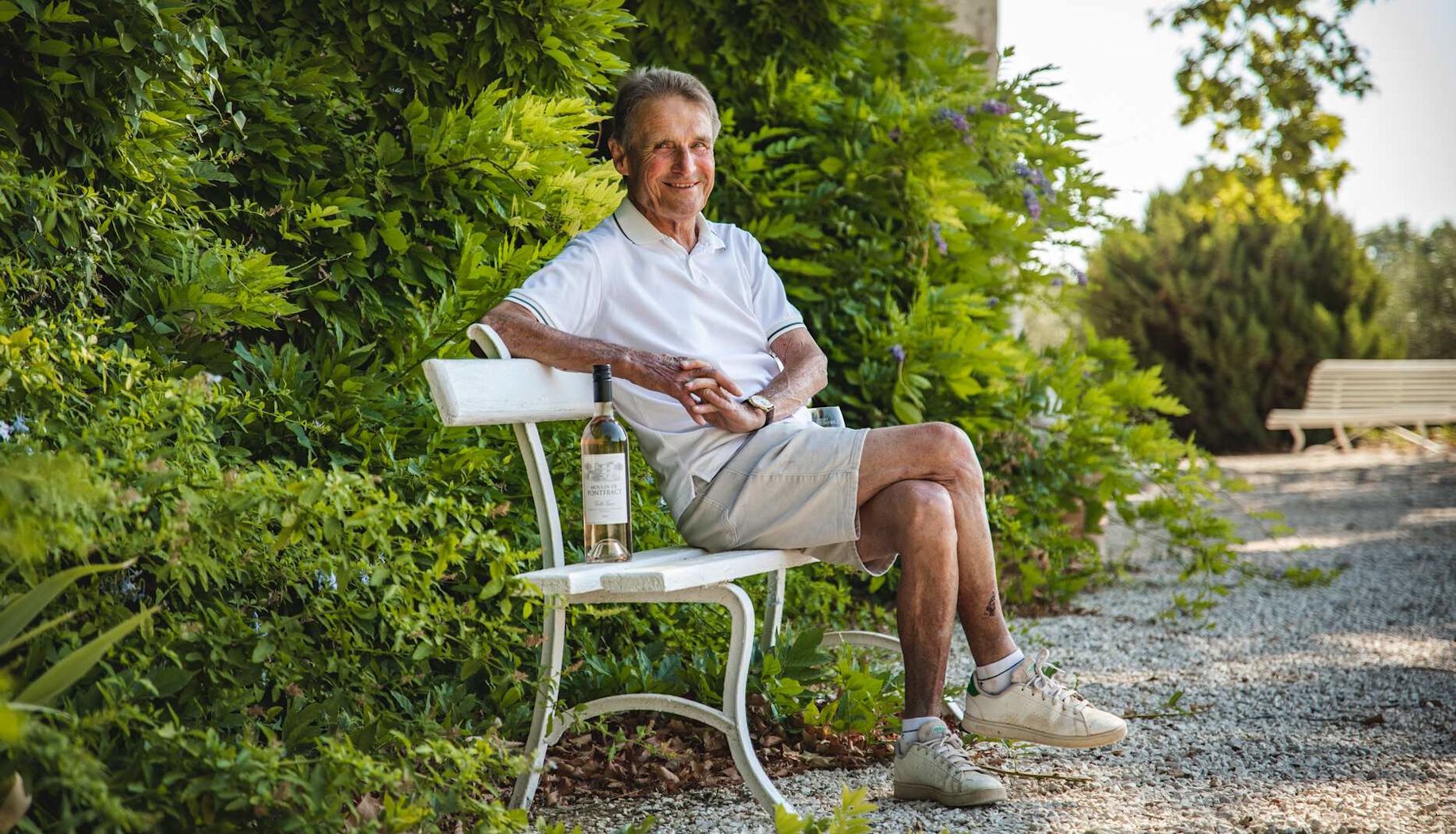 Winemaker, Monsieur Paul, sits on a bench with his Provence rosé wine
