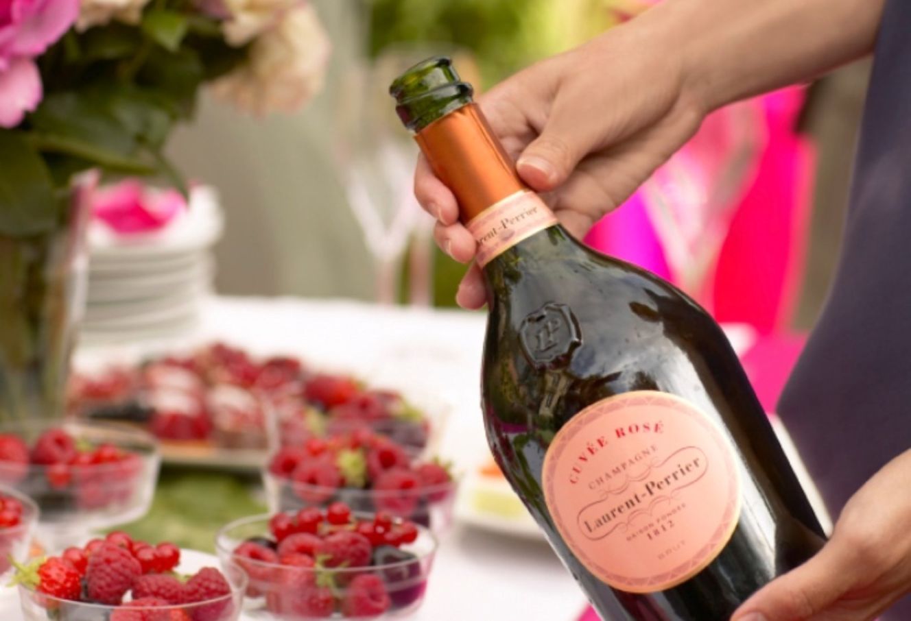 Person holding bottle of pink Champagne with table and flowers