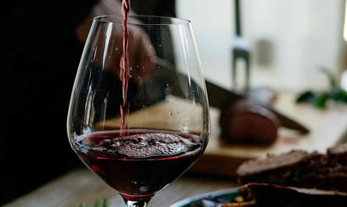 Red wine being poured into glass with meat being carved in the background