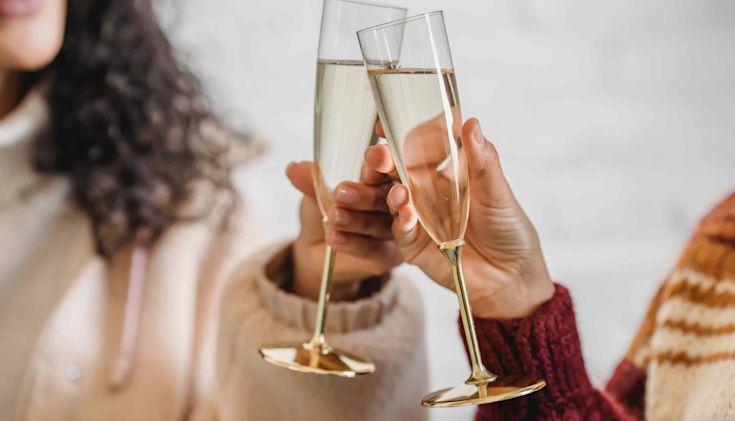 two women wearing jumpers clinking champagne flutes together