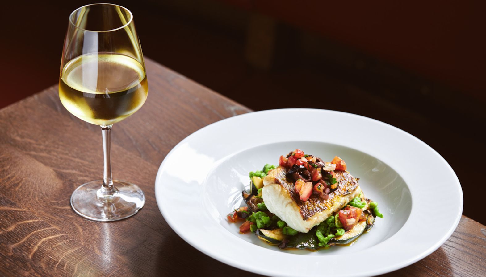 A glass of white wine next to a plate of cod and vegetables - wine with fish
