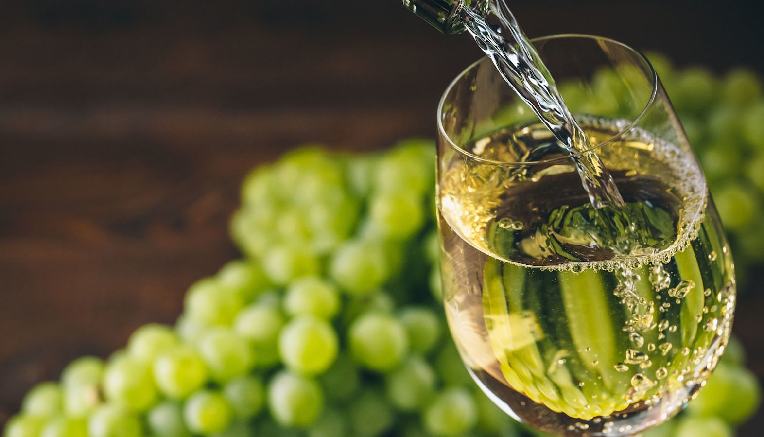 White wine being poured into a glass with green grapes in the background - best wine with pizza