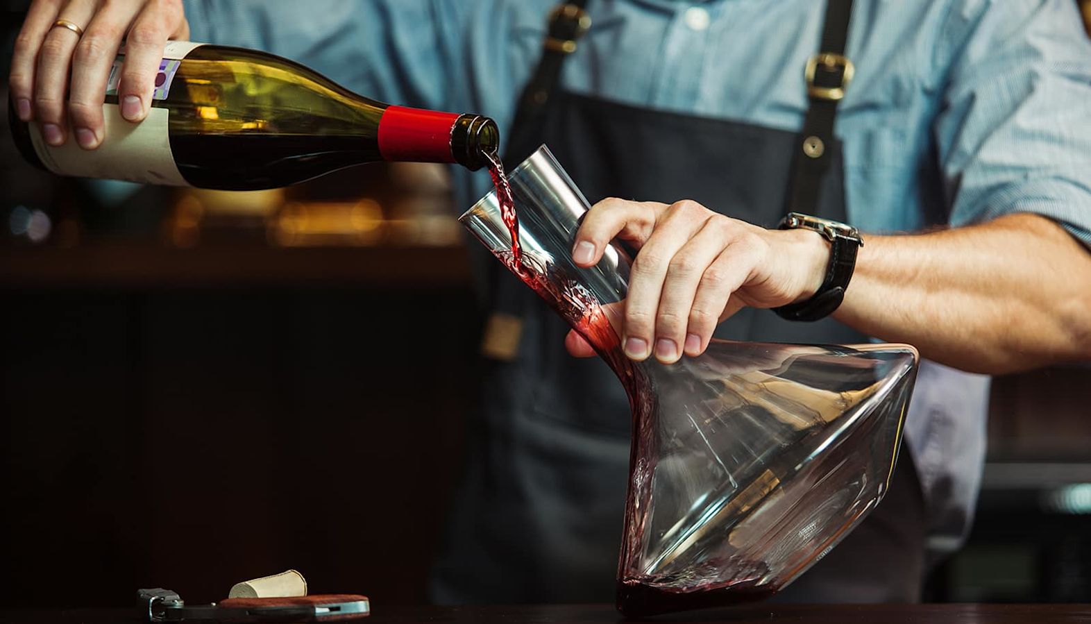 A bottle of red wine being poured into a decanter - decanting a wine