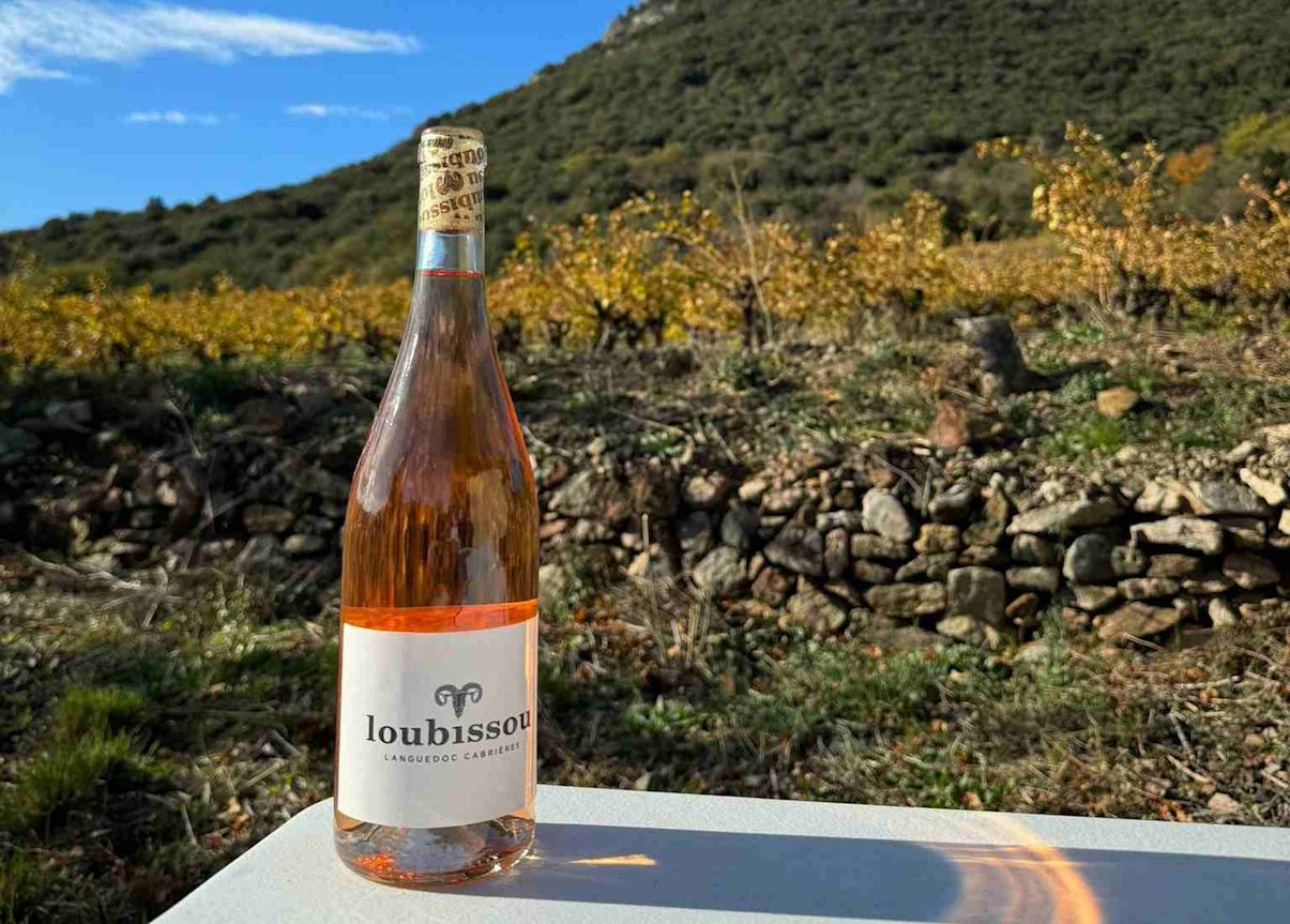 A bottle of Loubissou rosé sitting in a French vineyard