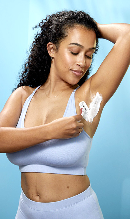 Young woman with curly hair shaving armpit with Gillette Venus razor