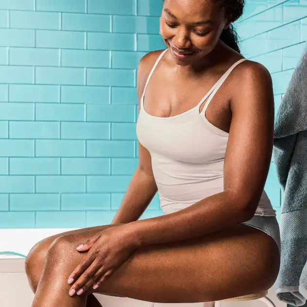 Femme assise dans une salle de bain, qui passe sa main sur sa jambe à la peau douce après un rasage.