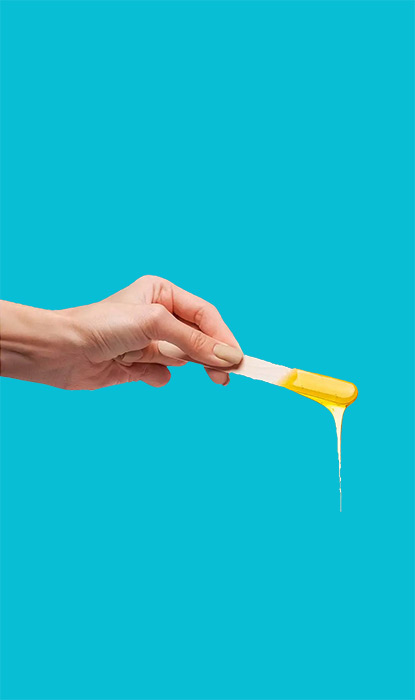 Hand holding a wooden spatula with dripping yellow wax