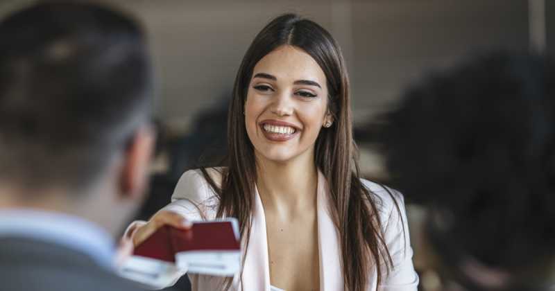 Eine lächelnde Frau im Blazer hält während eines Treffens mit zwei anderen Personen eine Visitenkarte hoch.