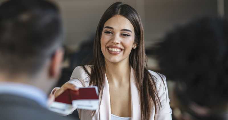 Eine lächelnde Frau im Blazer überreicht jemandem während eines Meetings eine Visitenkarte.