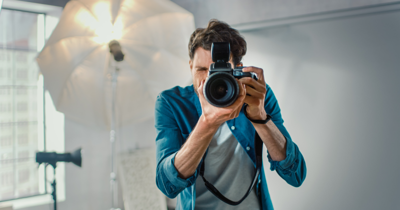Ein männlicher Fotograf verwendet eine professionelle Kamera in einem Studio mit einem Lichtschirm im Hintergrund.