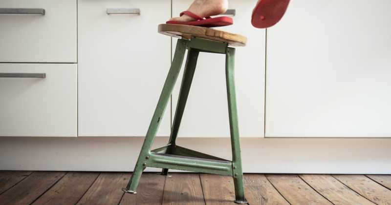 Person, die rote Flip-Flops trägt, steigt in einer Küche auf einen grünen Metallhocker.