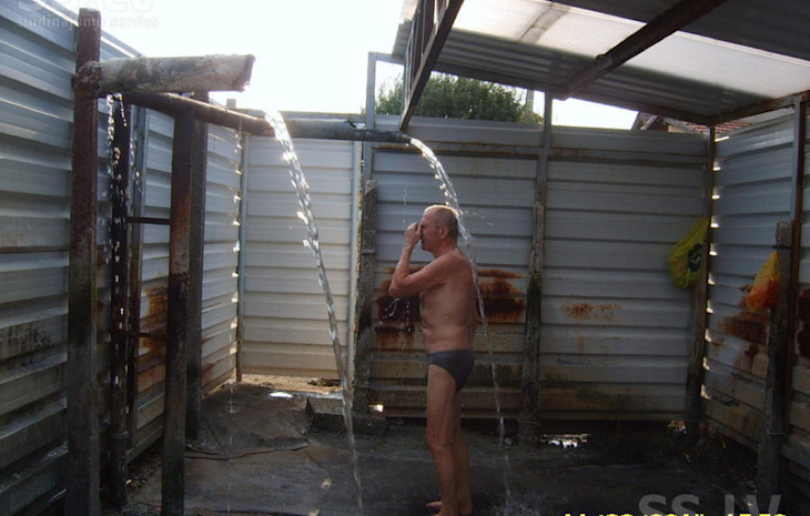 An old man using an outdoor shower in his underpants