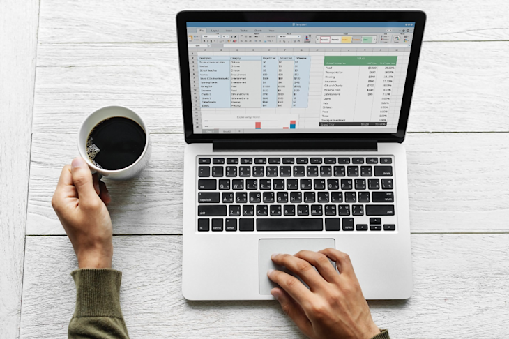 A man working on a computer and holding a coffee