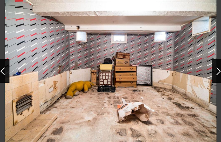 An abandoned cellar with some furniture and a large teddy bear in the corner