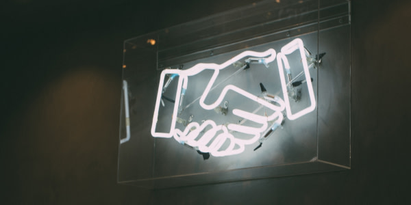 Ein Zeichen aus Neonröhren, das einen Händedruck oder einen Handschlag zeigt.