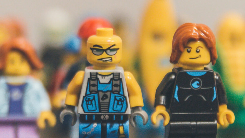 Zwei Lego-Figuren stehen nebeneinander - eine schmunzelt schelmisch, eine blickt kampfeslustig drein.