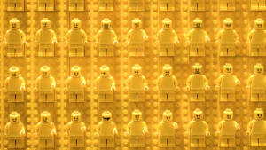 27 goldgelbe Lego-Figuren mit verschiedenen Gesichtsausdrücken liegen in drei Reihen nebeneinander auf goldgelbem Untergrund