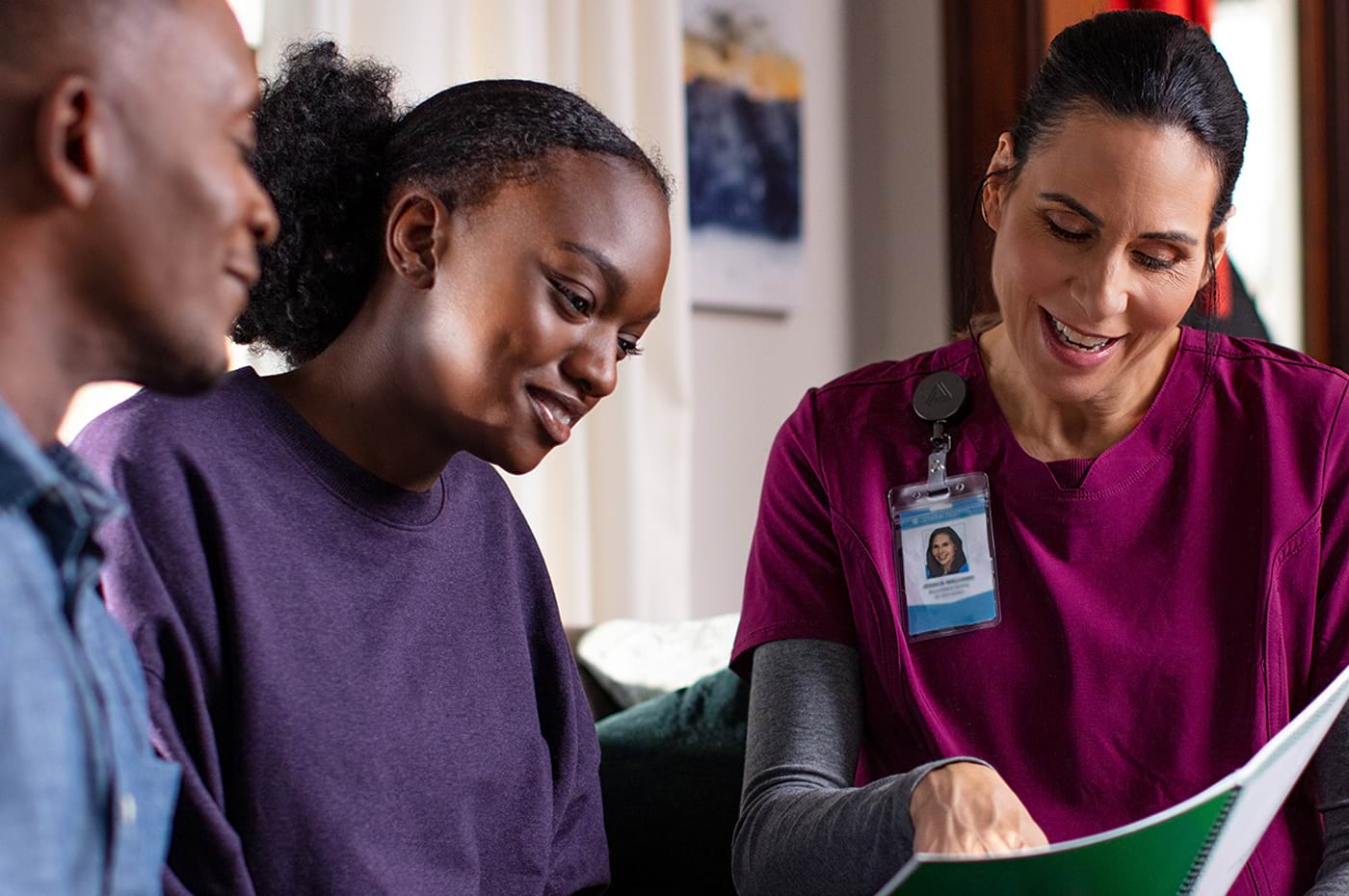 A healthcare professional is sitting down with a young adult and their father. They are smiling and looking at a pediatric clinical trial brochure. 