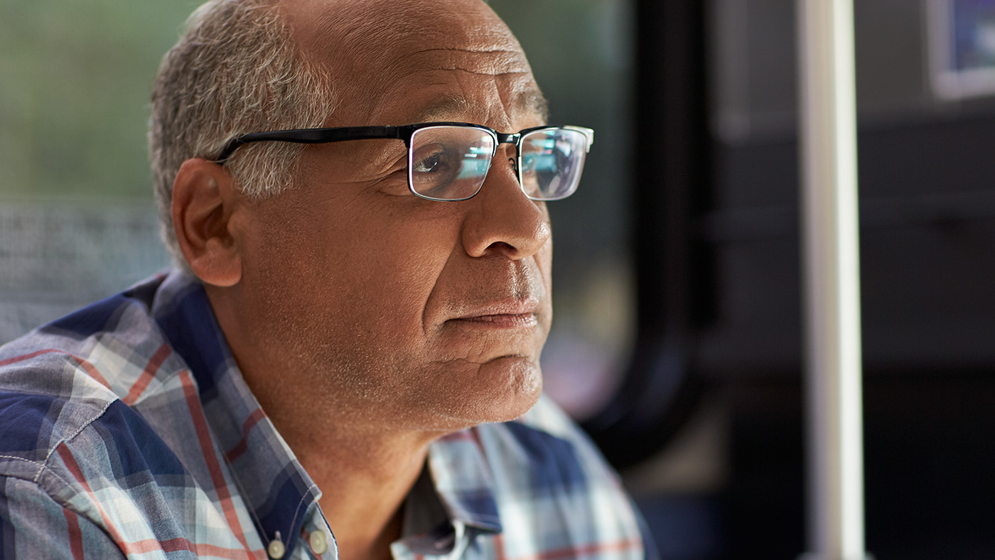An adult wearing glasses and a check shirt sitting down and looking at something out of shot. His expression is thoughtful.