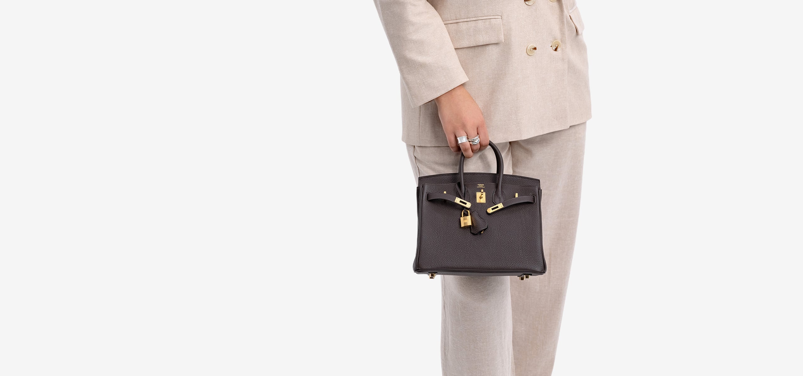 a woman in a beige suit holding a brown Hermes Birkin 25