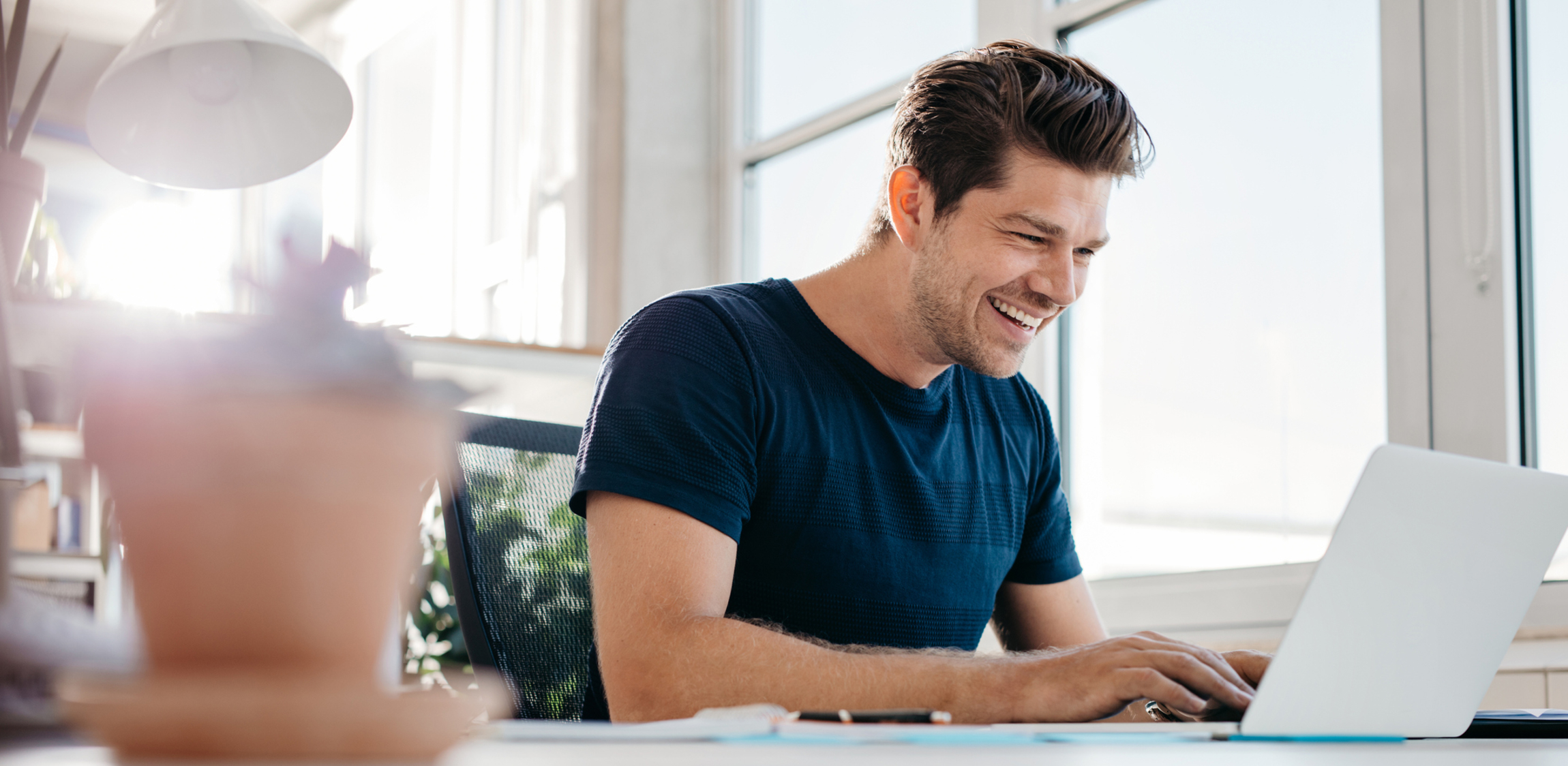 Een man zit in het thuiskantoor aan zijn bureau naast een groot raam